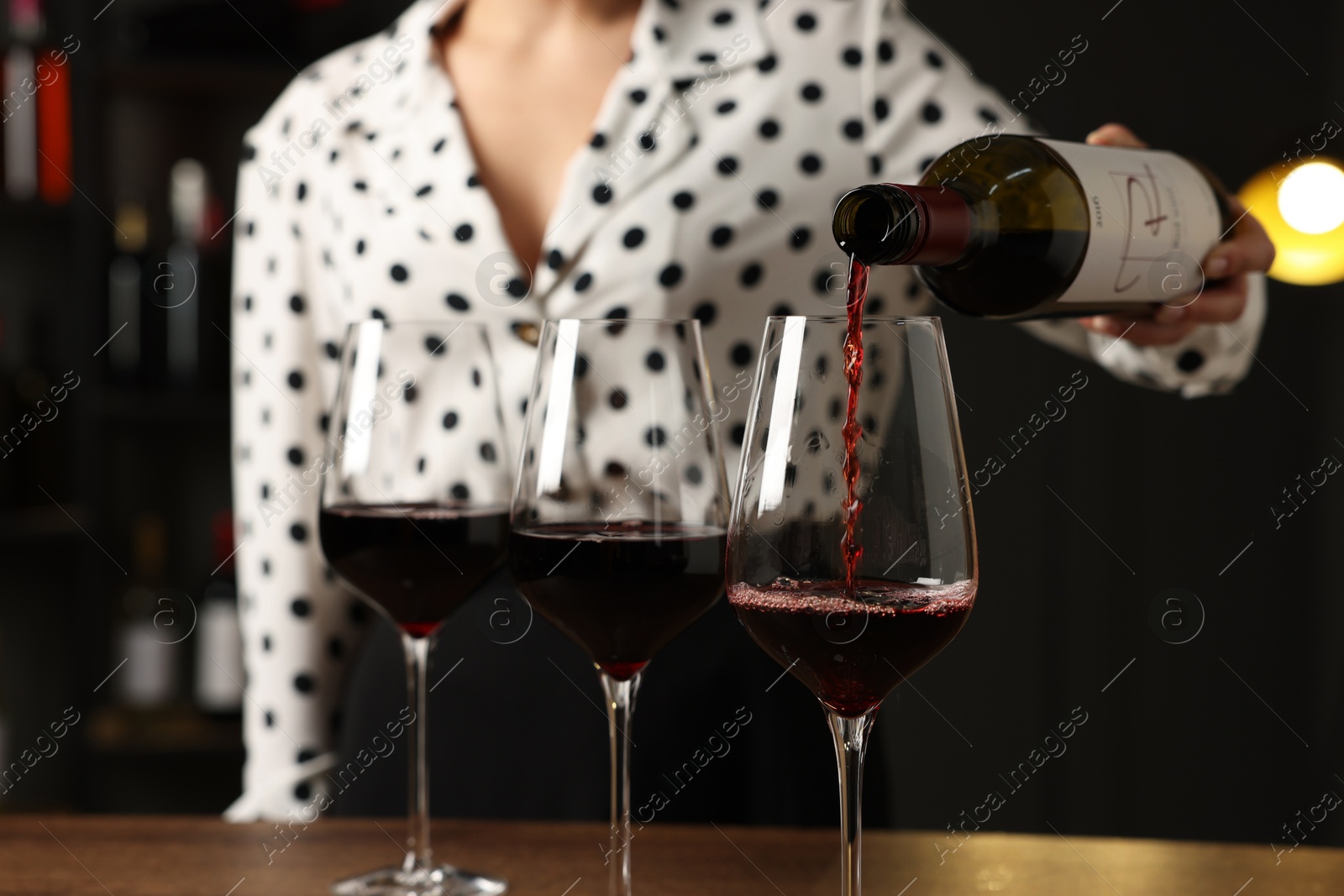 Photo of Professional sommelier pouring red wine into glasses at wooden table indoors, closeup