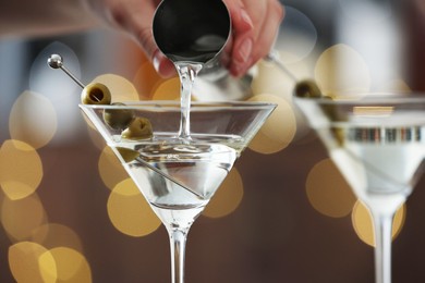 Photo of Woman making tasty martini cocktail with olives on blurred background, closeup. Bokeh effect