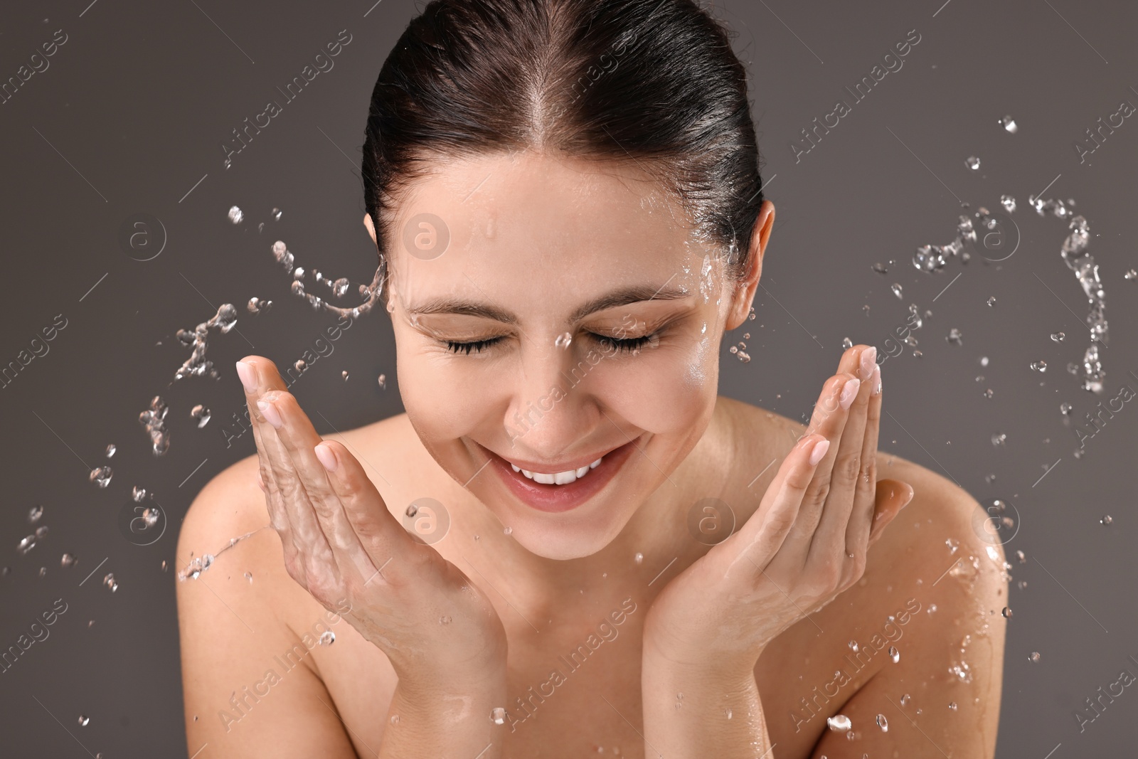 Photo of Smiling woman washing her face on grey background