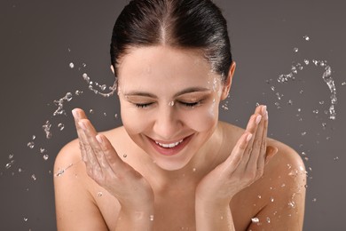 Photo of Smiling woman washing her face on grey background