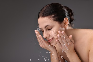 Attractive woman washing her face on grey background, space for text