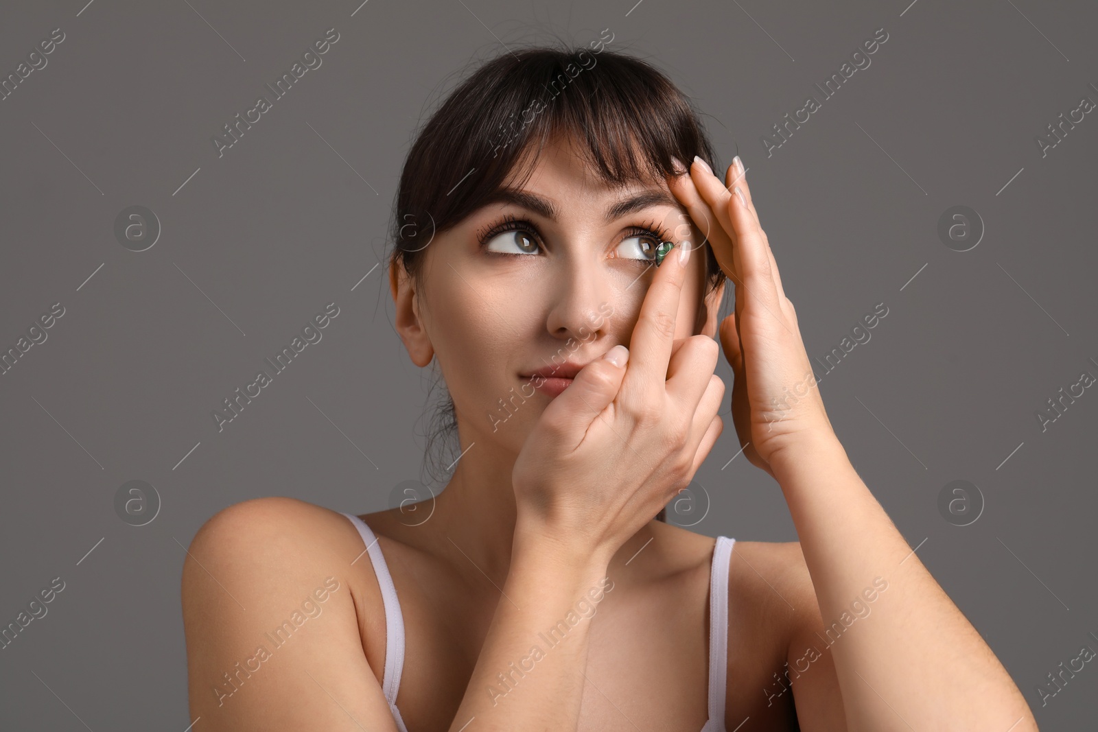 Photo of Young woman putting in green color contact lens on grey background