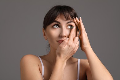 Photo of Young woman putting in green color contact lens on grey background