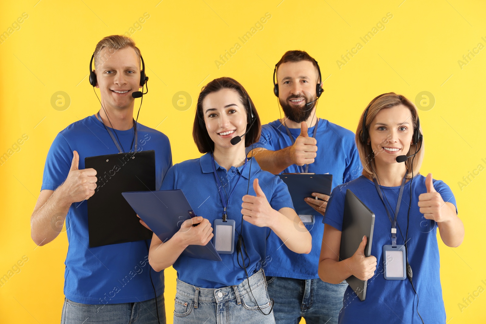 Photo of Technical support call center. Team of friendly operators showing thumbs up on yellow background