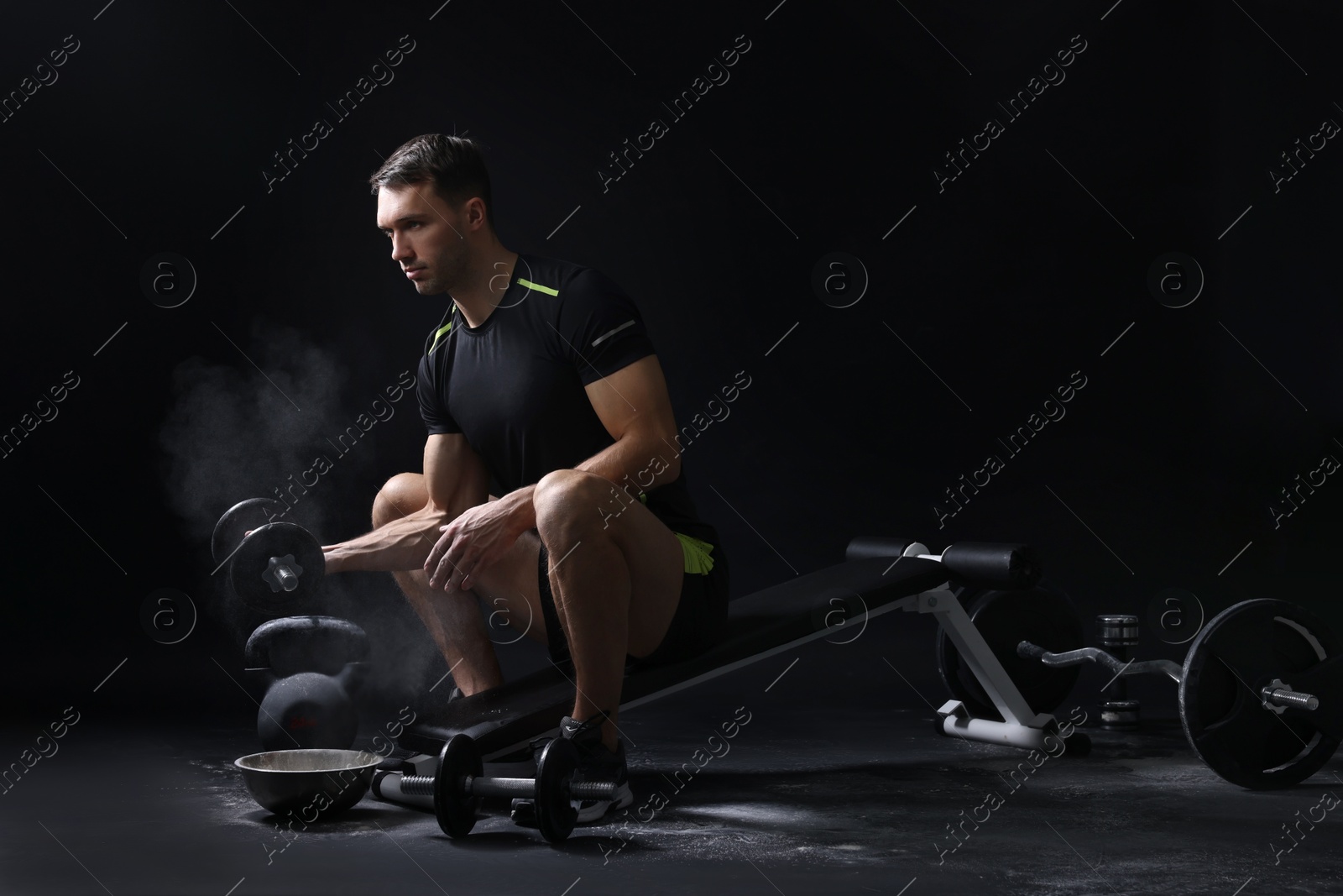 Photo of Man with talcum powder on hands training with barbell against black background