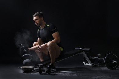 Photo of Man with talcum powder on hands training with barbell against black background