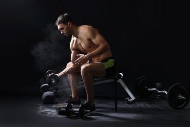 Man with talcum powder on hands training with barbell against black background