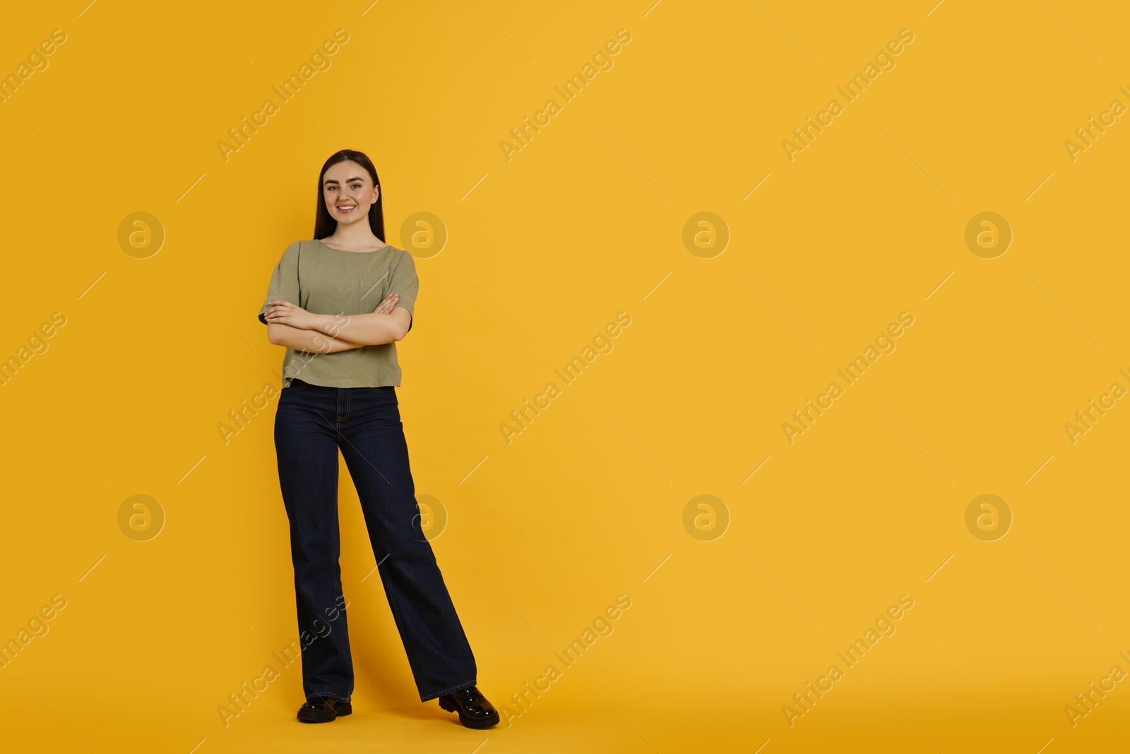 Photo of Smiling woman in stylish jeans on orange background. Space for text