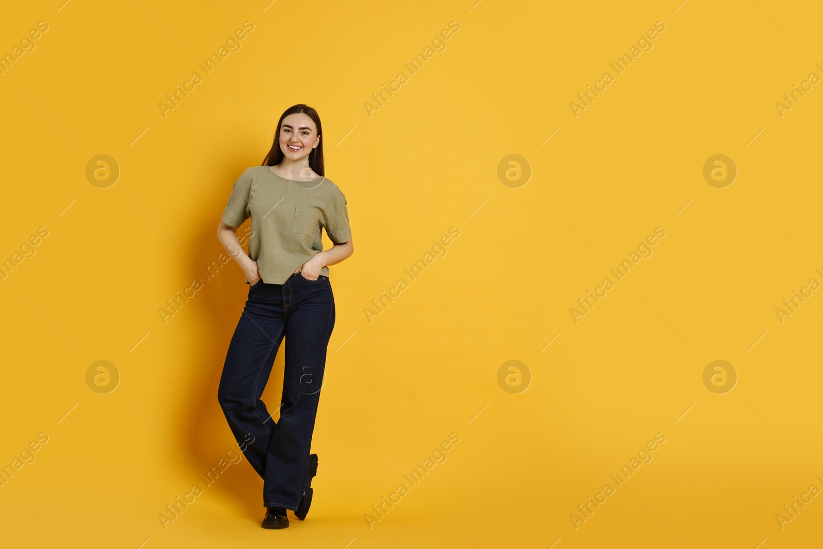 Photo of Smiling woman in stylish jeans on orange background. Space for text