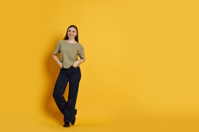 Photo of Smiling woman in stylish jeans on orange background. Space for text