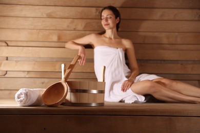 Photo of Beautiful woman relaxing on bench at sauna, focus on bath supplies