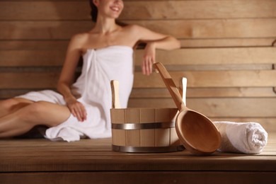 Photo of Smiling woman relaxing on bench at sauna, focus on bath supplies