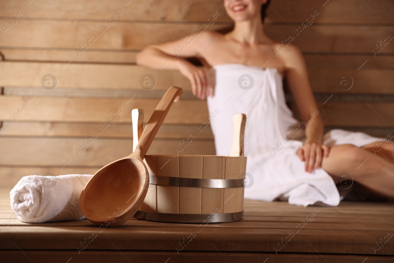 Photo of Smiling woman relaxing on bench at sauna, focus on bath supplies