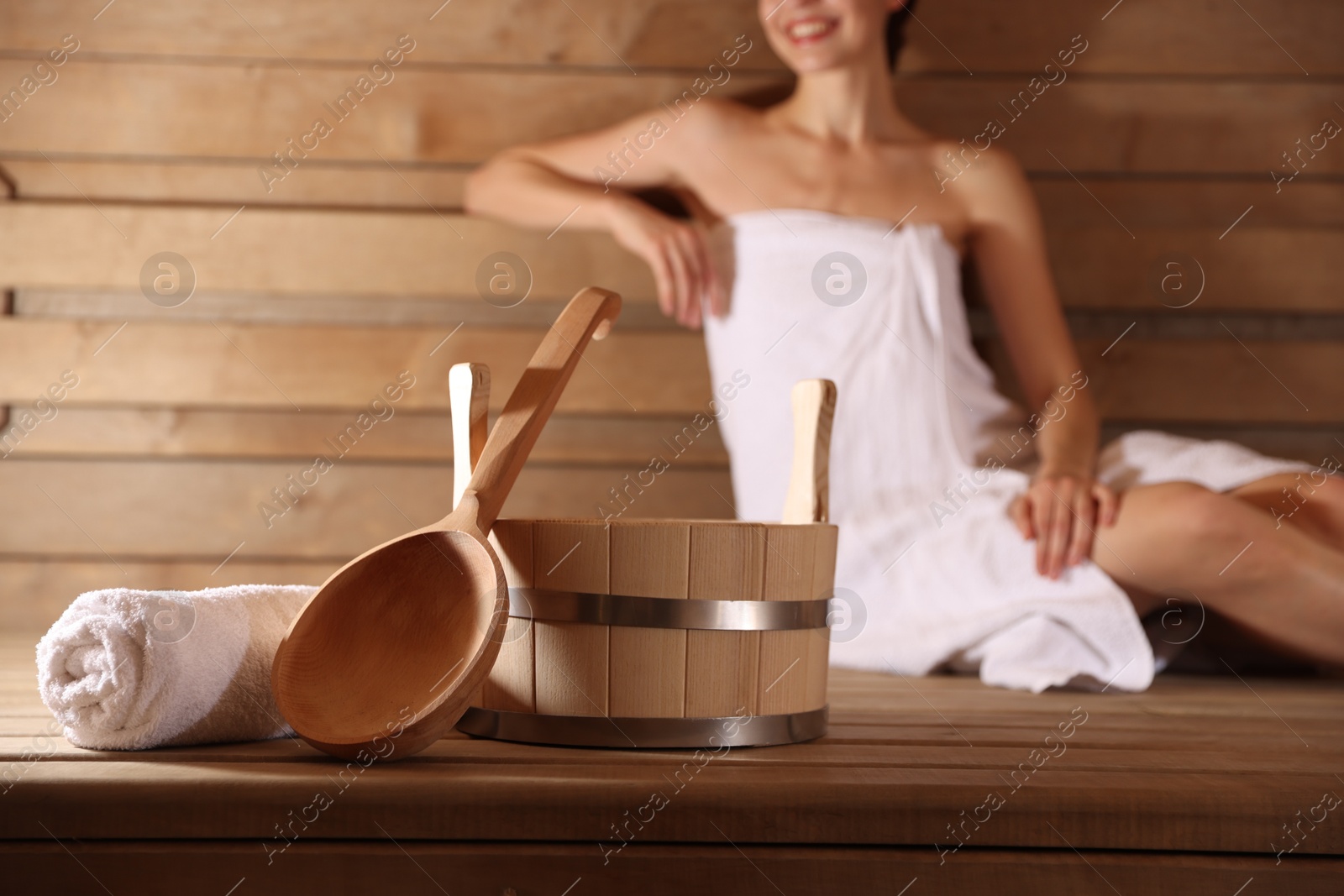 Photo of Smiling woman relaxing on bench at sauna, focus on bath supplies