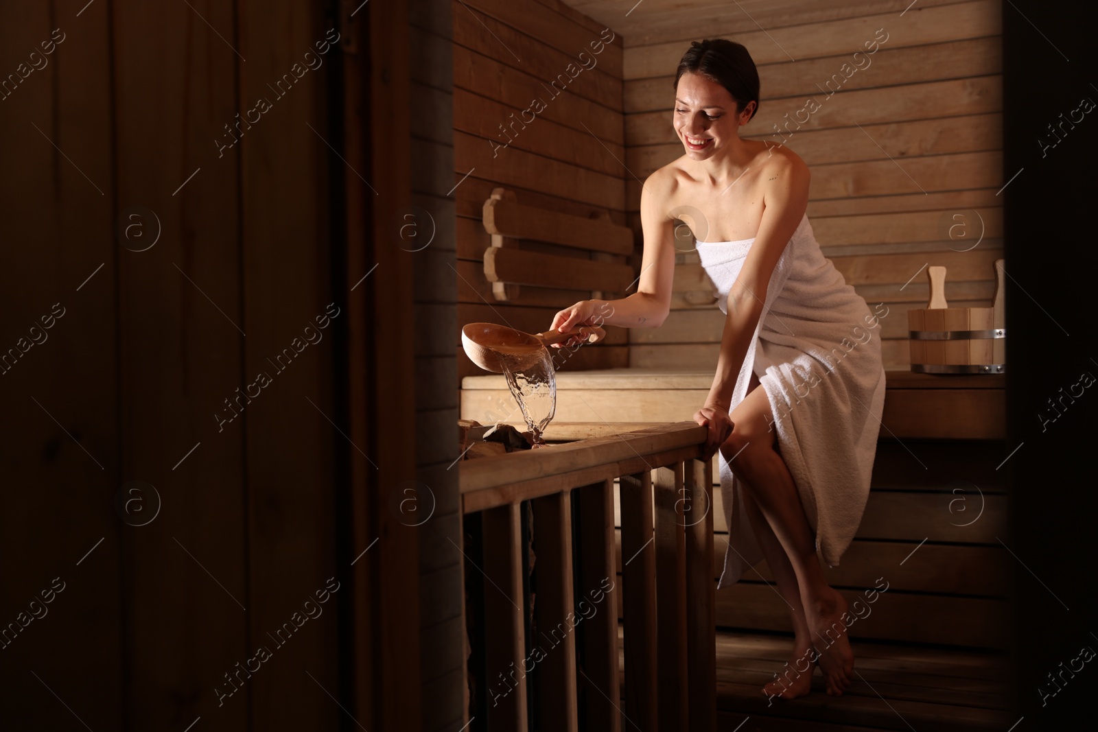 Photo of Smiling woman pouring water onto stones in sauna. Space for text