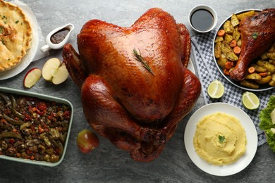 Photo of Whole baked turkey and other dishes served on grey table, flat lay