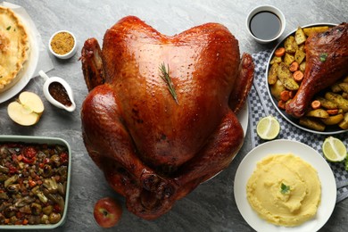 Photo of Whole baked turkey and other dishes served on grey table, flat lay