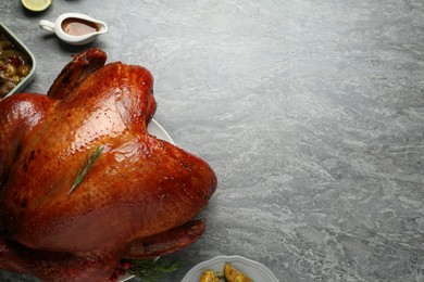 Photo of Whole baked turkey and other dishes served on grey table, flat lay. Space for text