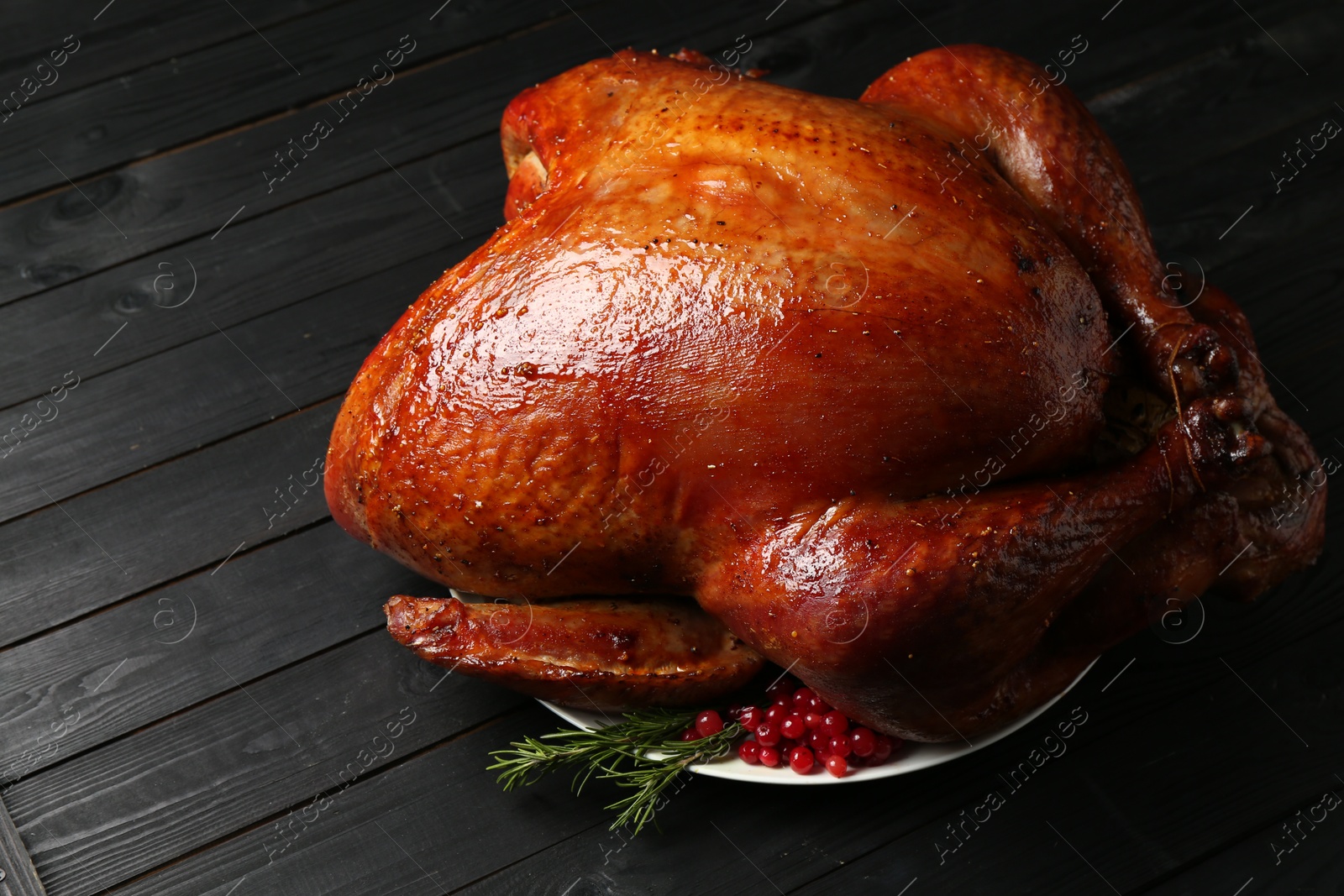 Photo of Whole baked turkey with cranberries and rosemary on black wooden table, closeup