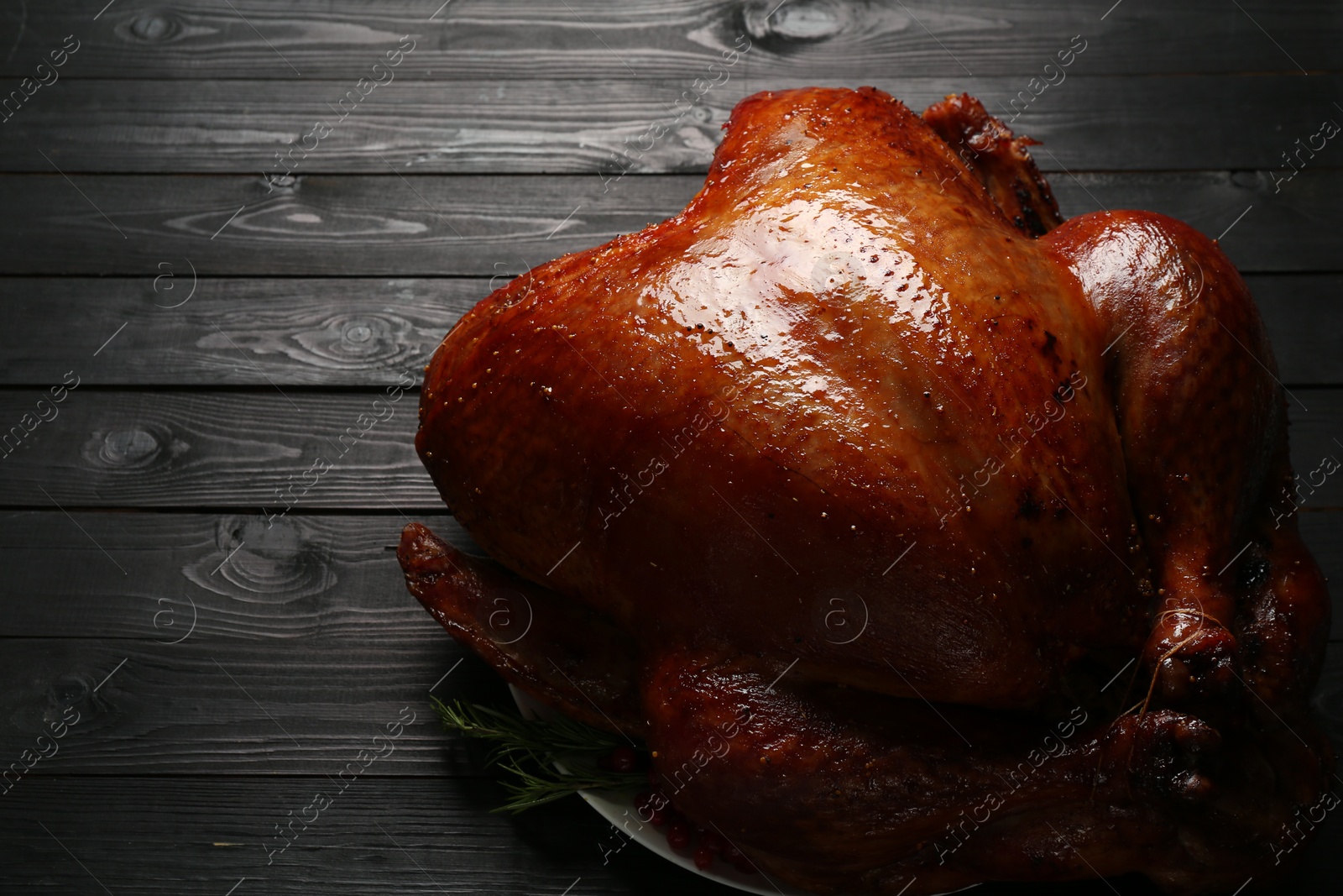 Photo of Whole baked turkey on black wooden table, closeup