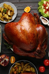 Photo of Whole baked turkey and other dishes served on black wooden table, flat lay