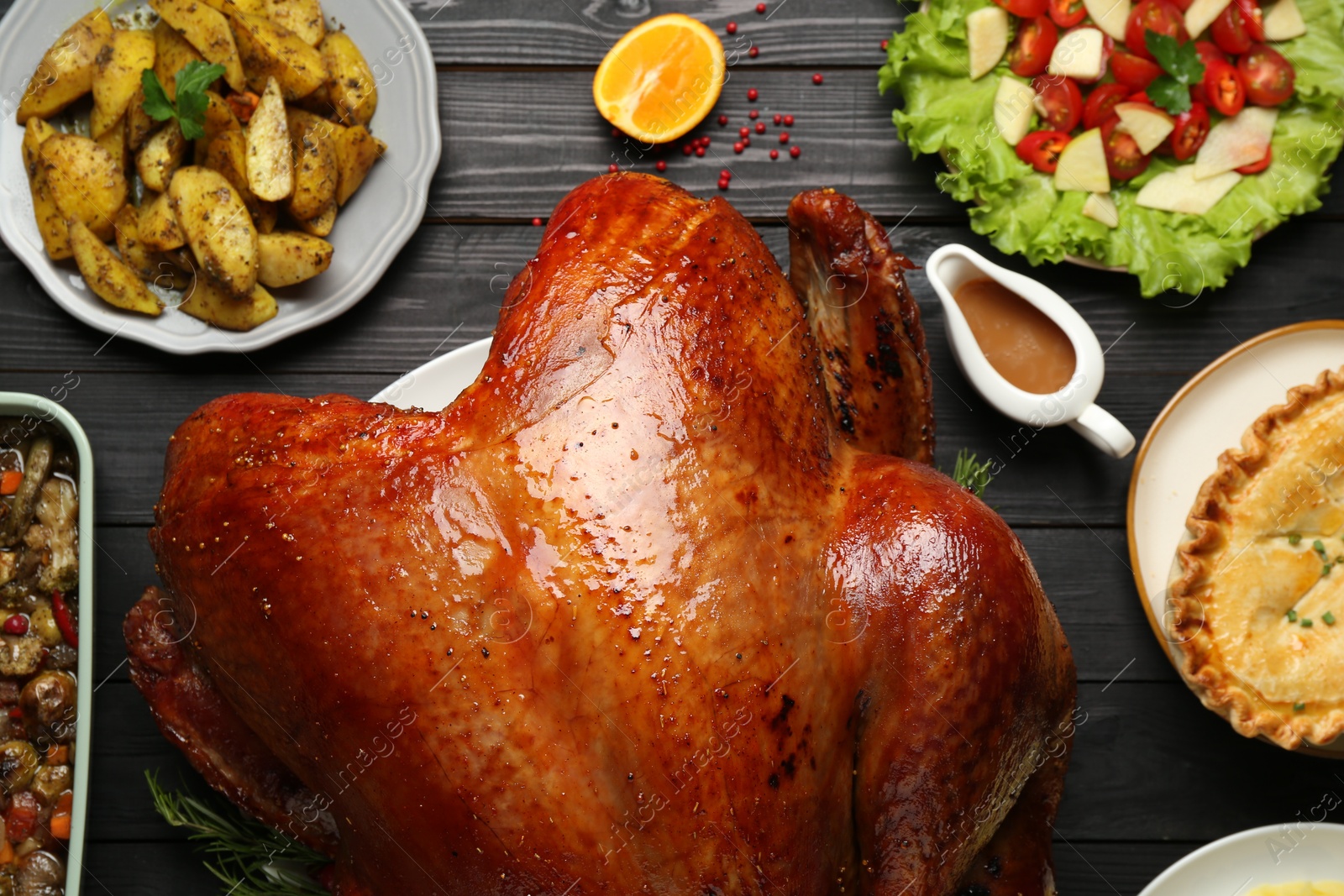 Photo of Whole baked turkey and other dishes served on black wooden table, flat lay