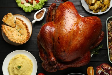 Photo of Whole baked turkey and other dishes served on black wooden table, flat lay