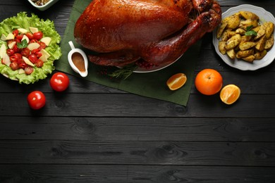 Photo of Whole baked turkey and other dishes served on black wooden table, flat lay. Space for text