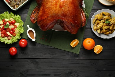 Photo of Whole baked turkey and other dishes served on black wooden table, flat lay. Space for text