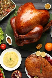 Photo of Whole baked turkey and other dishes served on black wooden table, flat lay