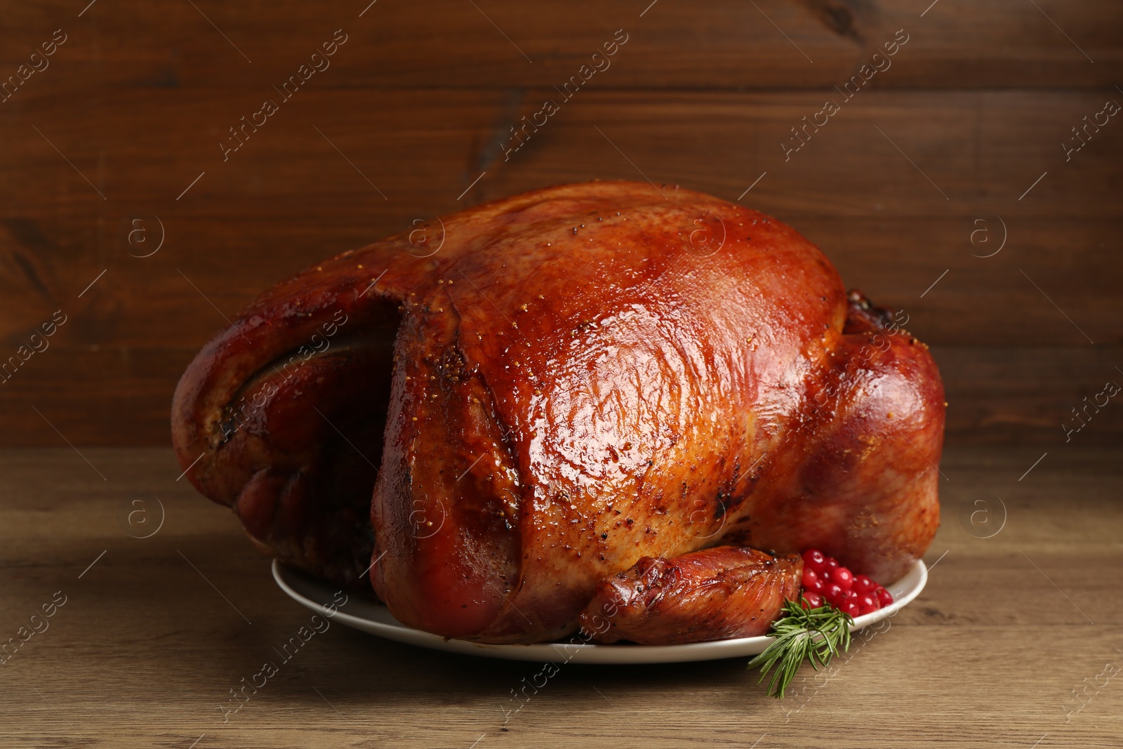 Photo of Whole baked turkey with cranberries and rosemary on wooden table, closeup