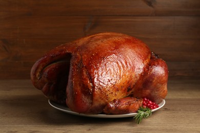 Photo of Whole baked turkey with cranberries and rosemary on wooden table, closeup