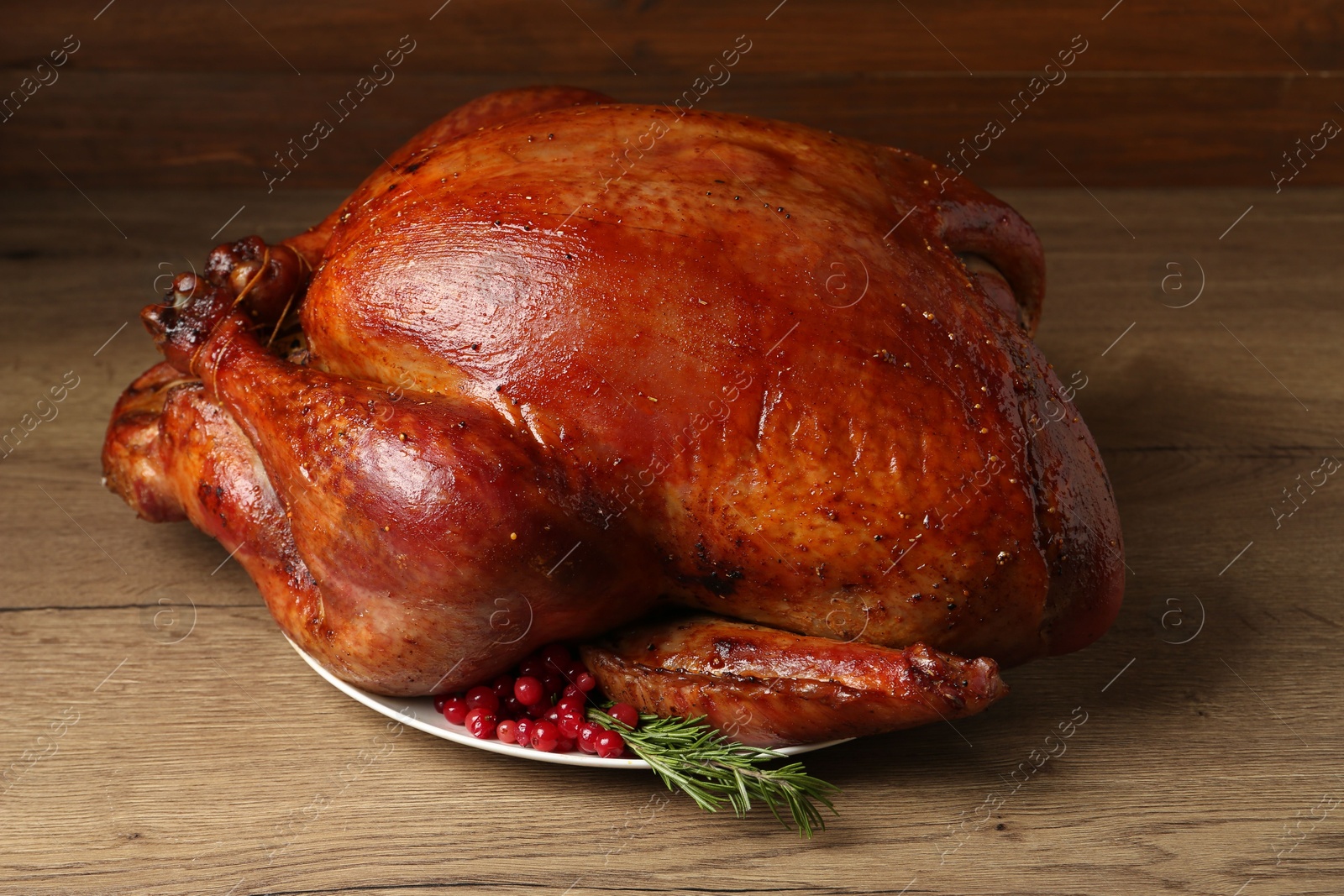 Photo of Whole baked turkey with cranberries and rosemary on wooden table, closeup