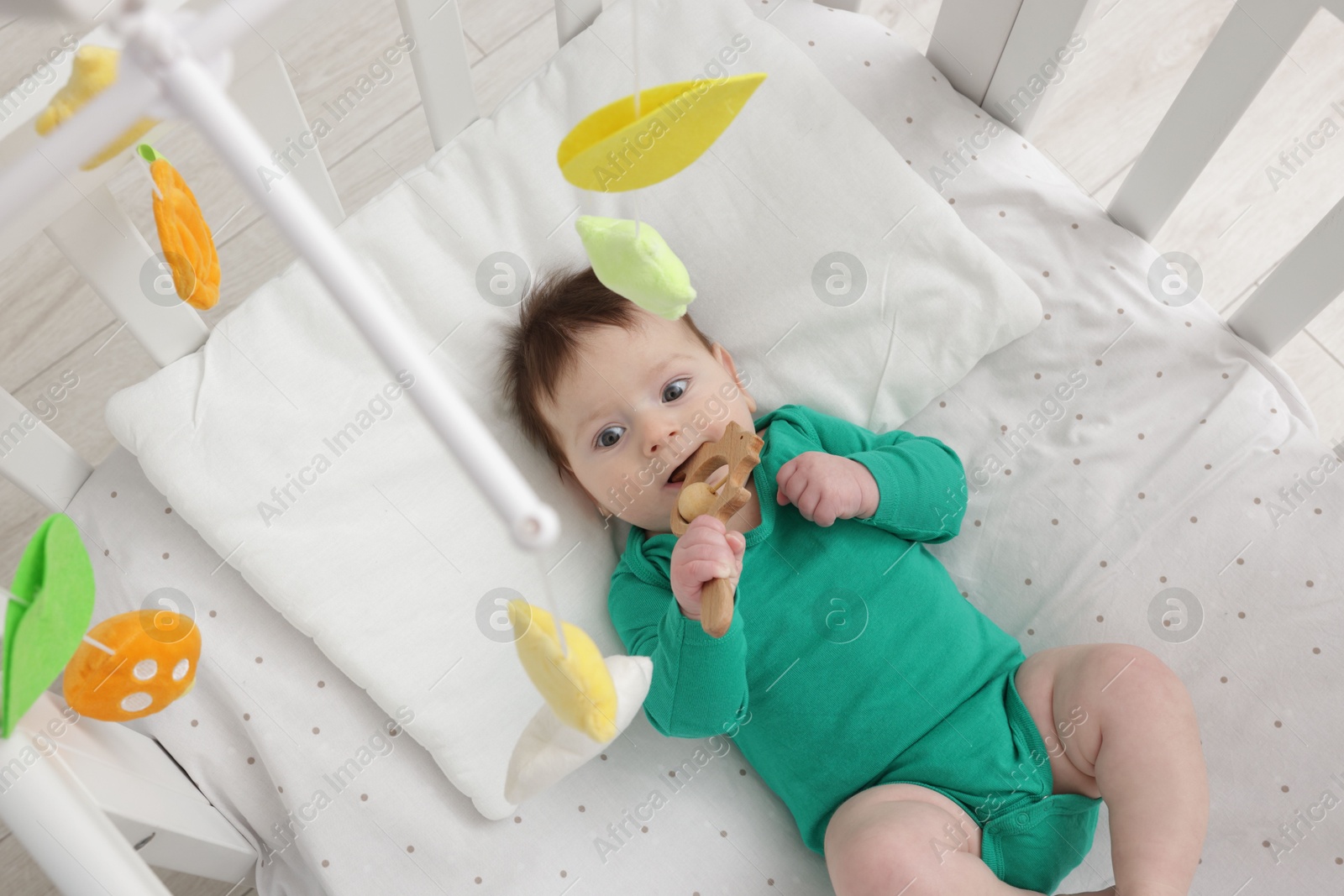 Photo of Cute little baby in crib with cot mobile at home, above view