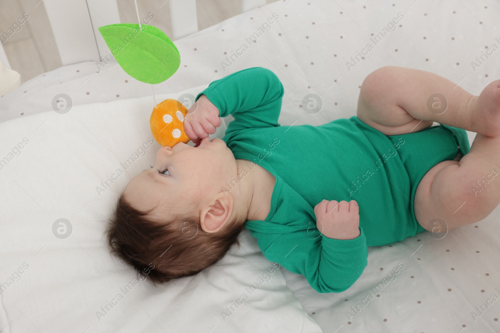 Photo of Cute little baby playing with cot mobile in crib at home