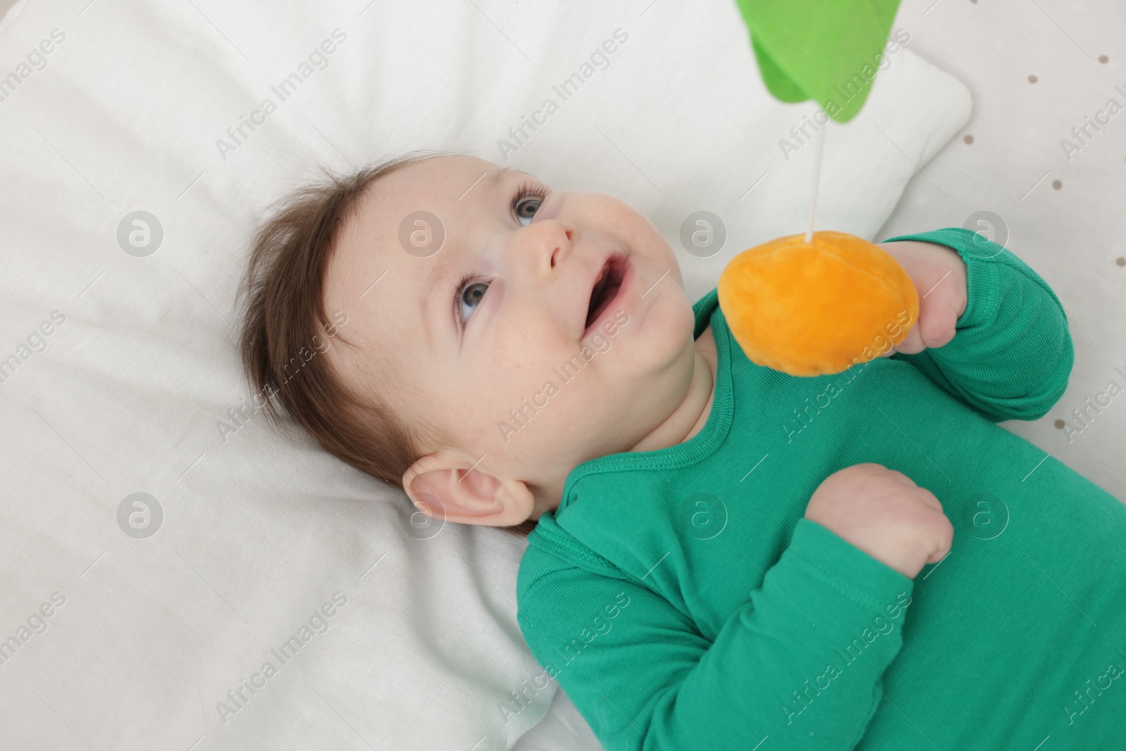 Photo of Cute little baby playing with cot mobile in crib at home