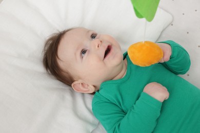 Photo of Cute little baby playing with cot mobile in crib at home