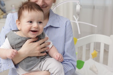 Photo of Mother holding her little baby, closeup. Crib with cot mobile in nursery