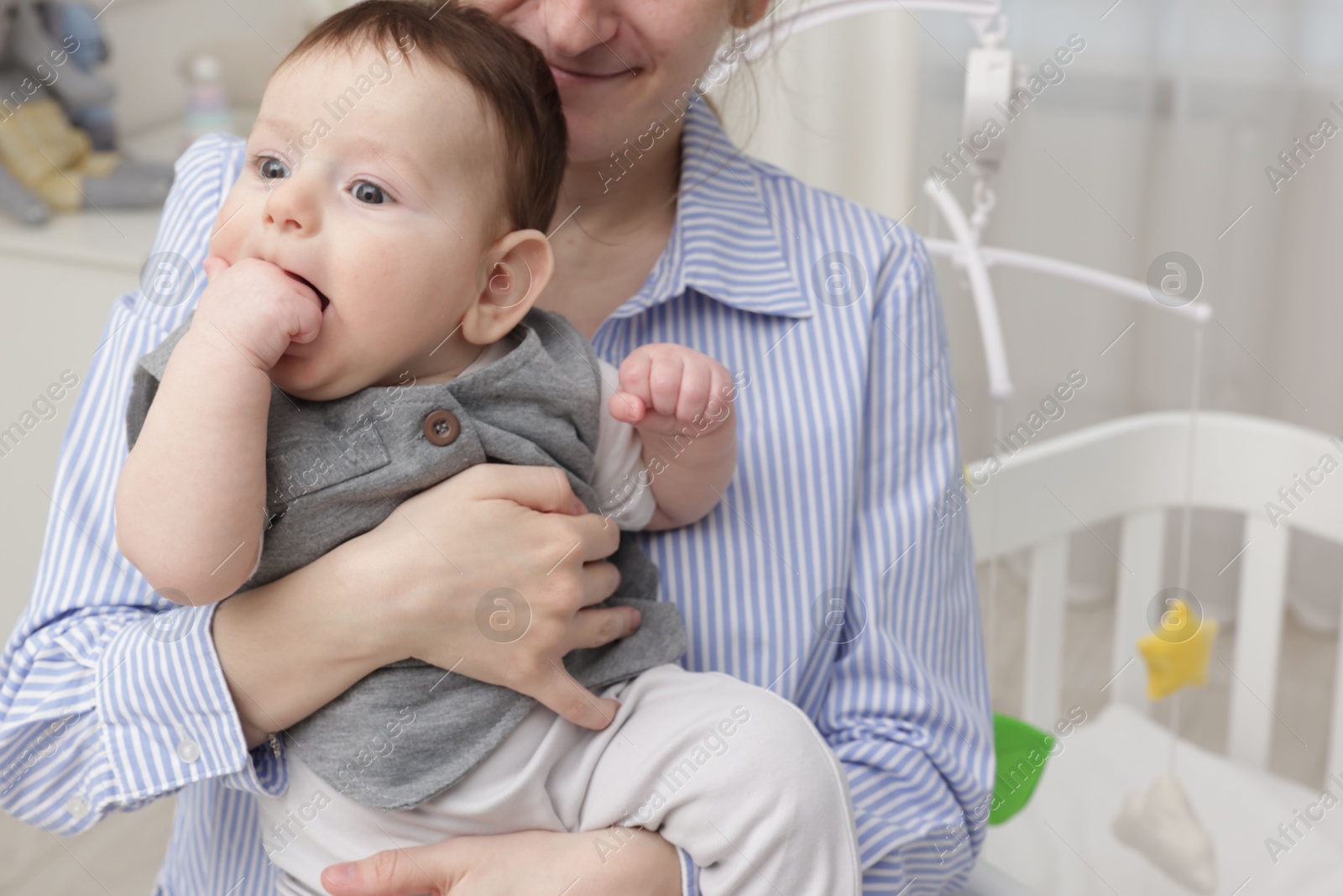 Photo of Mother holding her little baby, closeup. Crib with cot mobile in nursery