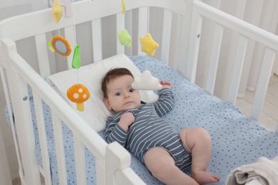 Photo of Cute little baby in crib with cot mobile at home