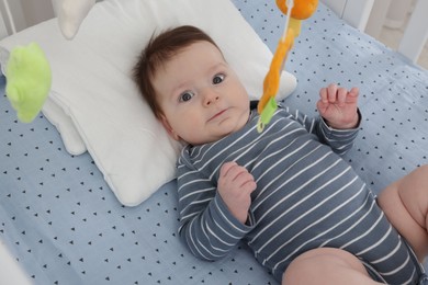 Photo of Cute little baby in crib with cot mobile at home