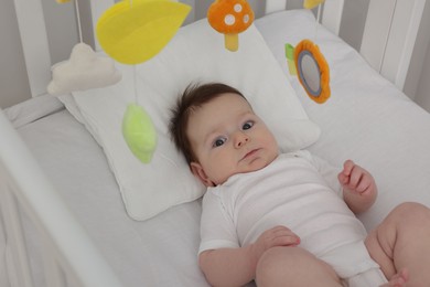 Photo of Cute little baby in crib with cot mobile at home