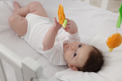 Photo of Cute little baby playing with cot mobile in crib at home