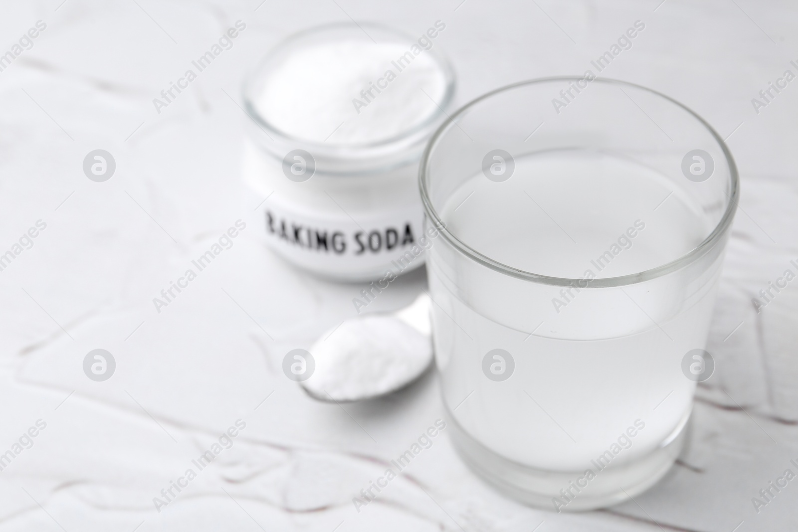 Photo of Glass with water and baking soda on white textured table, closeup