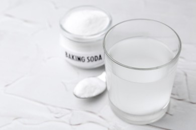 Photo of Glass with water and baking soda on white textured table, closeup