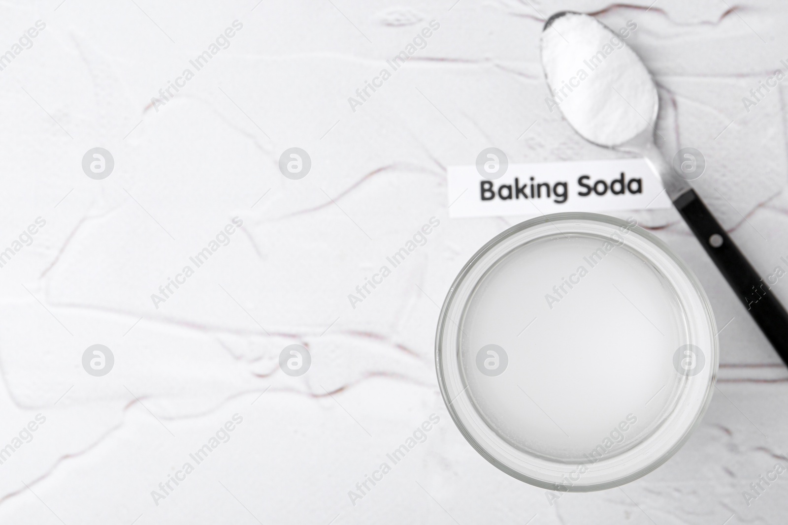 Photo of Glass with water and baking soda on white textured table, top view. Space for text