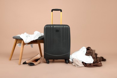 Photo of Suitcase with messy clothes, shoes and stool on beige background