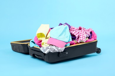 Photo of Packed suitcase full of clothes on light blue background