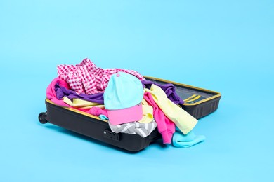 Photo of Packed suitcase full of clothes on light blue background