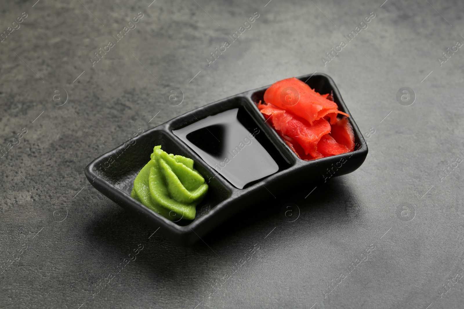 Photo of Hot wasabi paste, soy sauce and ginger on grey textured table, closeup